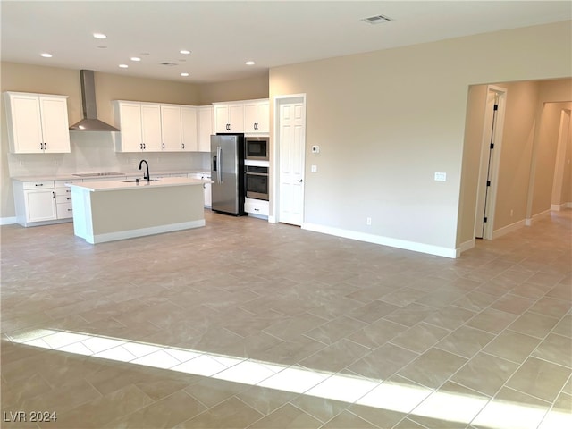 kitchen with stainless steel appliances, white cabinets, wall chimney exhaust hood, sink, and an island with sink