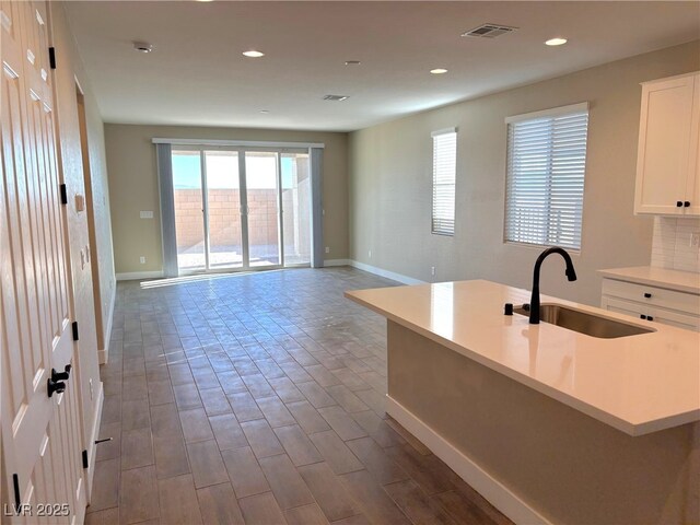 kitchen with decorative backsplash, white cabinetry, a kitchen island with sink, and sink