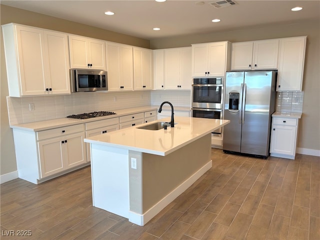 kitchen featuring stainless steel appliances, white cabinetry, a center island with sink, and sink