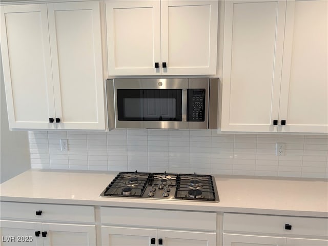 kitchen featuring gas cooktop, tasteful backsplash, white cabinetry, and light stone counters