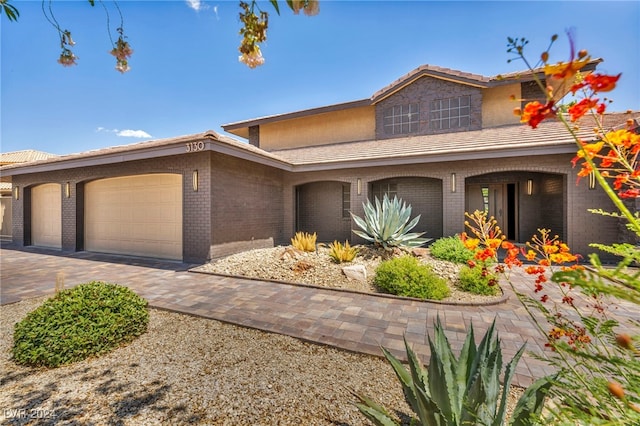 view of front facade featuring brick siding, a tiled roof, decorative driveway, and a garage