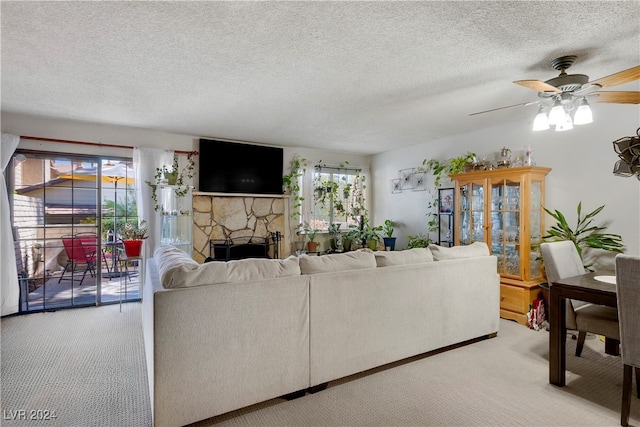 living room featuring a healthy amount of sunlight, ceiling fan, a stone fireplace, and carpet flooring