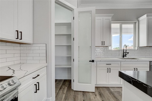 kitchen with stainless steel electric range oven, light wood-style flooring, a sink, and white cabinetry