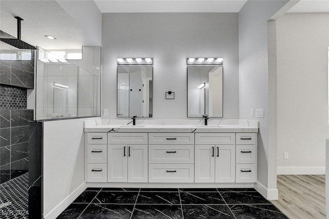 full bath featuring double vanity, baseboards, marble finish floor, walk in shower, and a sink