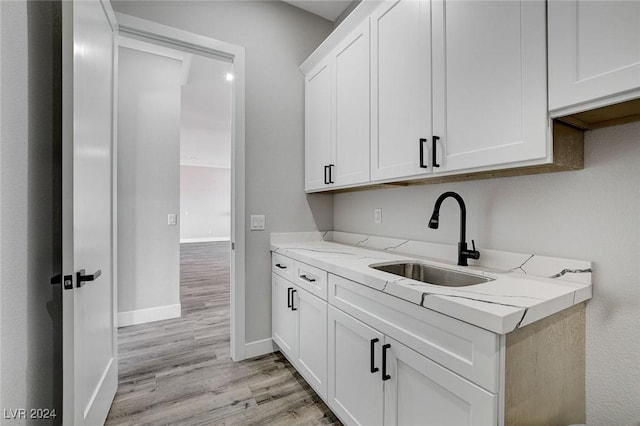 kitchen featuring light stone counters, light wood-type flooring, a sink, and white cabinets