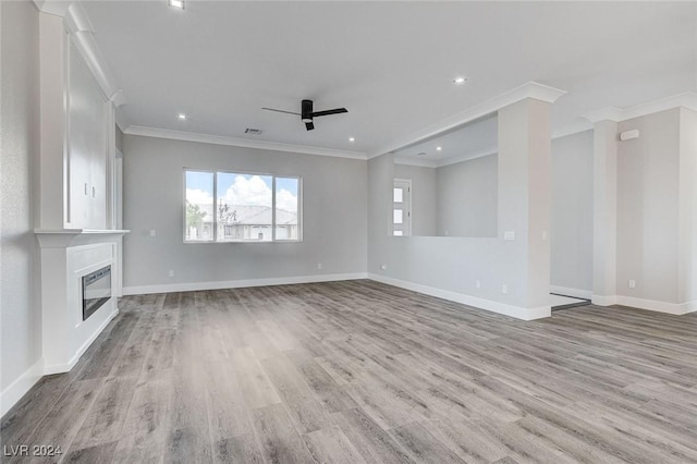 unfurnished living room with light wood-style floors, a glass covered fireplace, ornamental molding, a ceiling fan, and baseboards