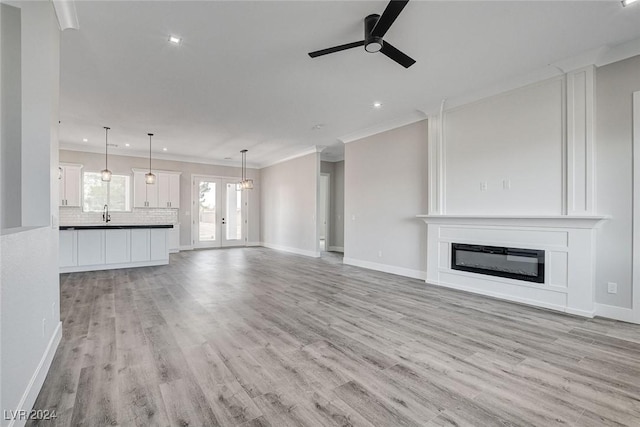 unfurnished living room with ceiling fan, light wood finished floors, a glass covered fireplace, and crown molding