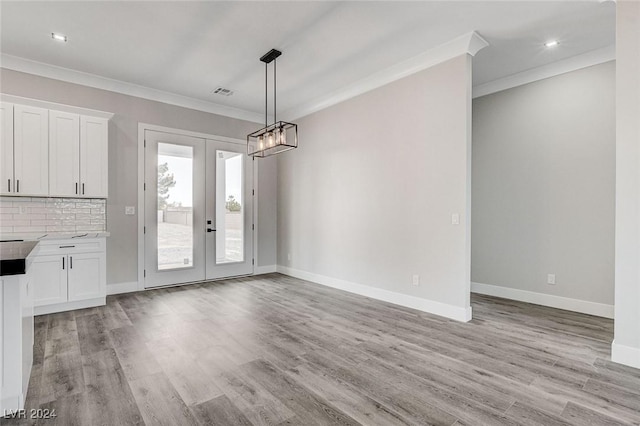 unfurnished dining area with light wood finished floors, french doors, ornamental molding, and baseboards