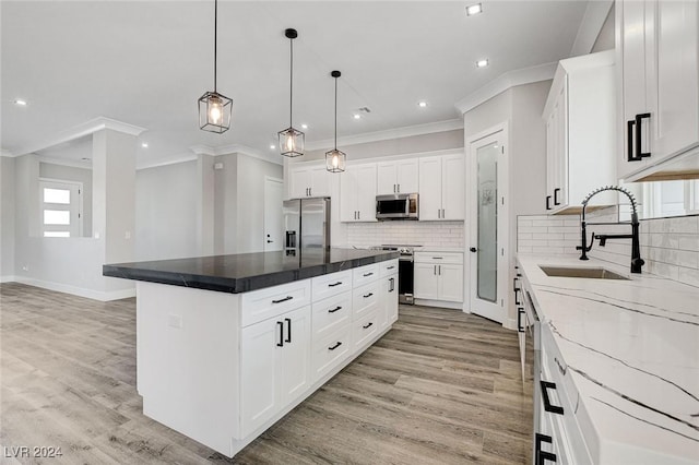 kitchen featuring stainless steel appliances, a sink, white cabinets, a center island, and decorative light fixtures