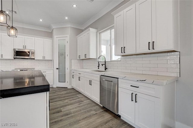 kitchen featuring stainless steel appliances, a sink, white cabinetry, hanging light fixtures, and light wood finished floors