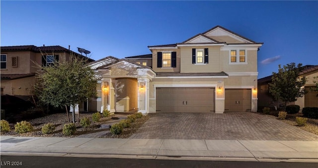 traditional-style home featuring decorative driveway, an attached garage, and stucco siding