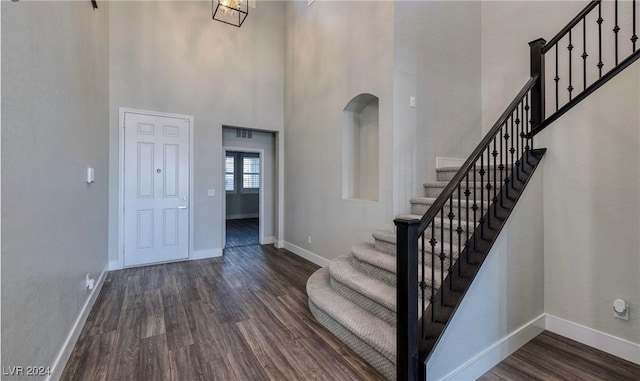 entrance foyer featuring a towering ceiling, stairway, baseboards, and dark wood finished floors