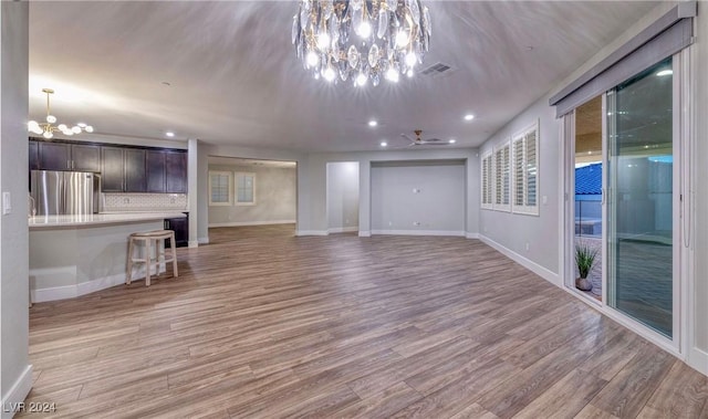 unfurnished living room featuring light wood-type flooring, baseboards, visible vents, and a notable chandelier