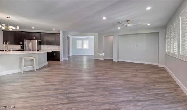 unfurnished living room with light wood-type flooring, ceiling fan with notable chandelier, and recessed lighting