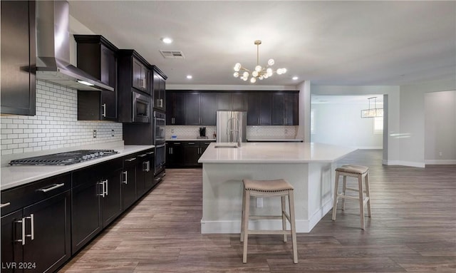 kitchen featuring stainless steel appliances, a breakfast bar, visible vents, wall chimney exhaust hood, and an inviting chandelier