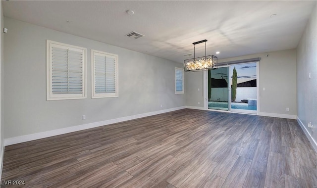 spare room with dark wood-style floors, a chandelier, visible vents, and baseboards