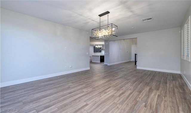 unfurnished living room with a notable chandelier, baseboards, visible vents, and wood finished floors