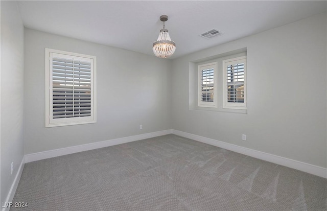 carpeted spare room featuring an inviting chandelier, visible vents, and baseboards