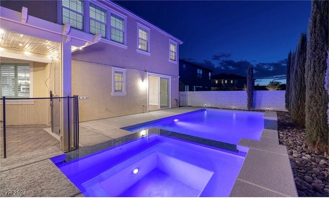 pool at night with a patio area, a fenced backyard, a fenced in pool, and an in ground hot tub