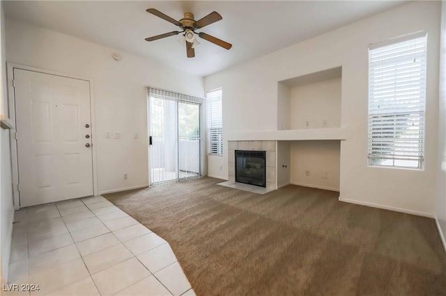 unfurnished living room featuring carpet floors, a fireplace, a ceiling fan, baseboards, and tile patterned floors