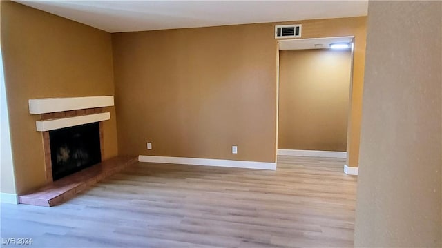 unfurnished living room with light wood-type flooring, a fireplace, visible vents, and baseboards