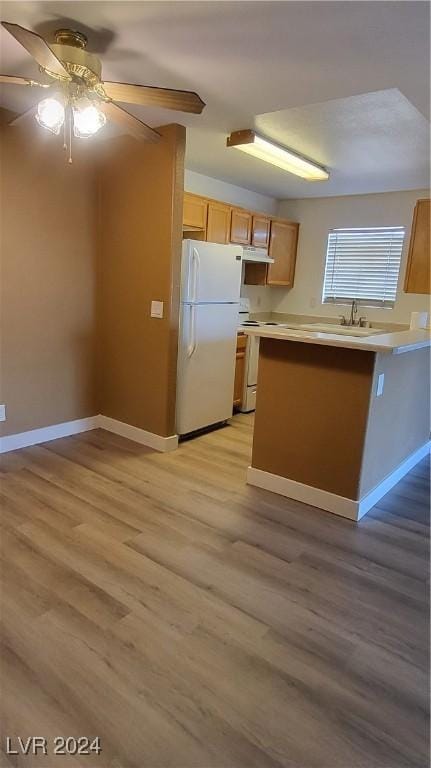 kitchen with white appliances, a peninsula, light countertops, light brown cabinetry, and light wood-type flooring