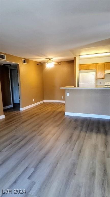 unfurnished living room featuring dark wood-type flooring, a ceiling fan, visible vents, and baseboards