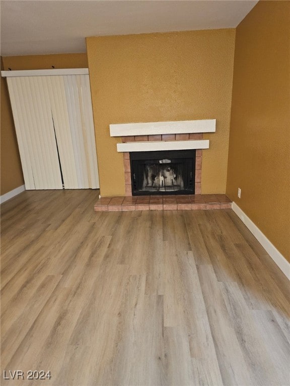 unfurnished living room with baseboards, a tiled fireplace, and wood finished floors