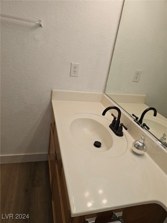 bathroom with a textured wall, vanity, baseboards, and wood finished floors