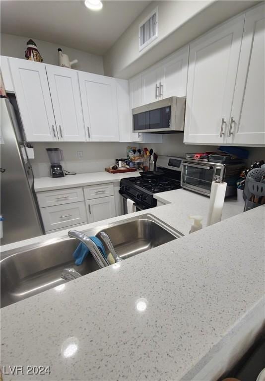 kitchen featuring light stone counters, a toaster, stainless steel appliances, visible vents, and white cabinetry