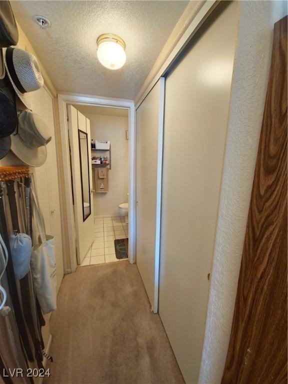 hall with a textured ceiling, light tile patterned floors, and light carpet