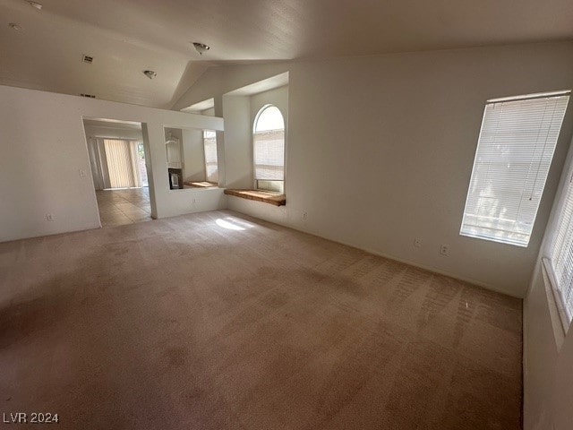 unfurnished room featuring a wealth of natural light, vaulted ceiling, and light carpet