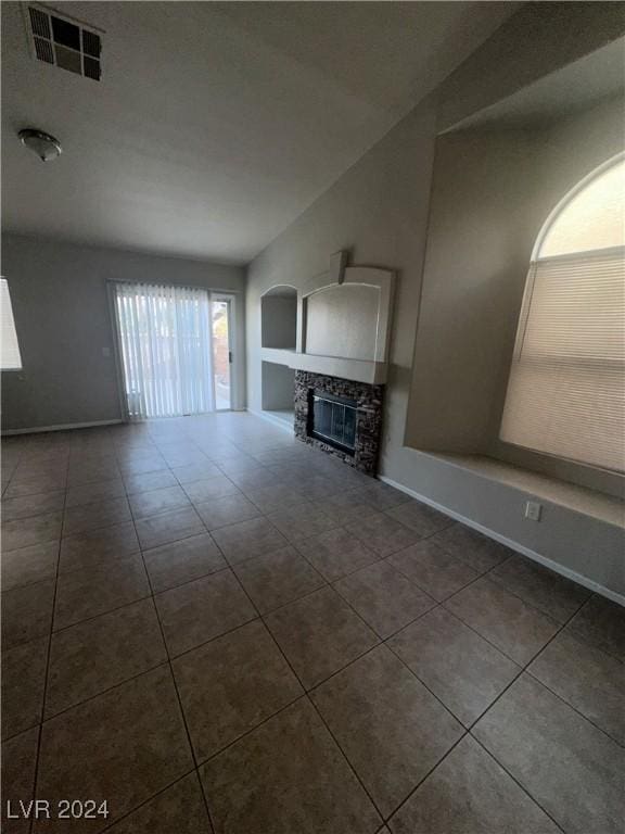 unfurnished living room featuring a stone fireplace, vaulted ceiling, and dark tile patterned floors