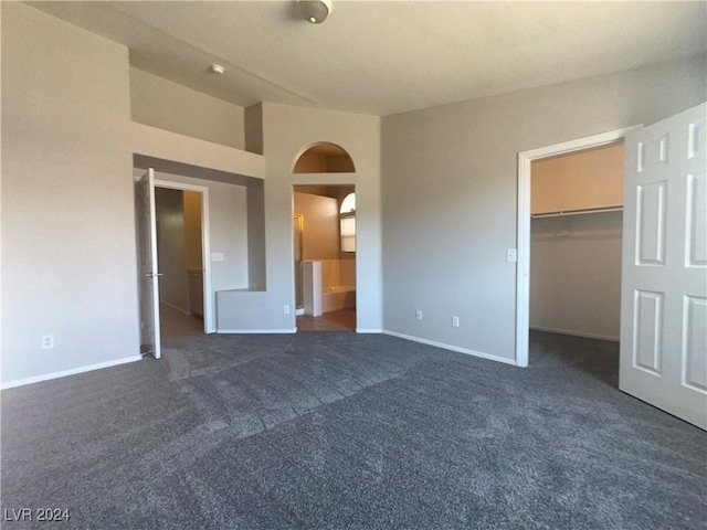 unfurnished bedroom featuring dark colored carpet, a walk in closet, and a closet