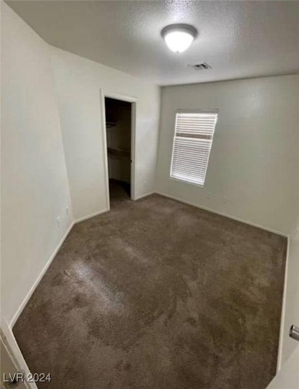 unfurnished bedroom with a spacious closet, a closet, carpet, and a textured ceiling