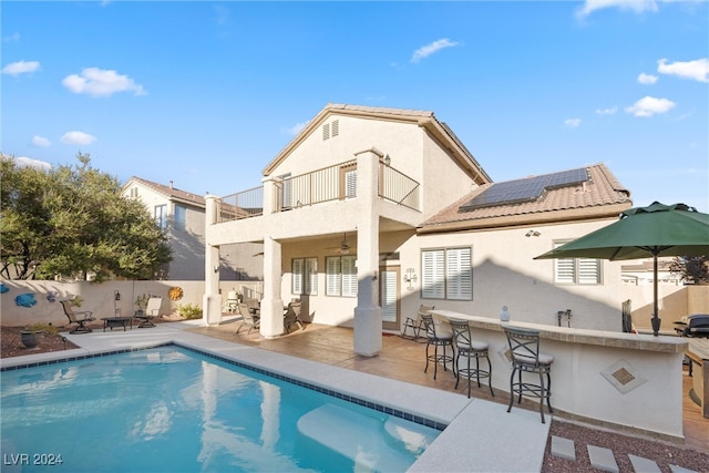 back of property featuring a bar, a patio, a fenced in pool, ceiling fan, and solar panels