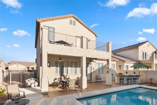 rear view of property featuring a patio, a balcony, an outdoor bar, and a fenced in pool