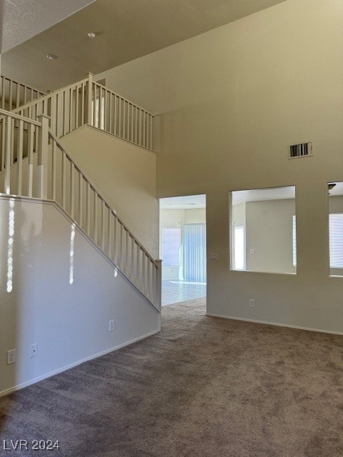 unfurnished living room with carpet flooring and a high ceiling