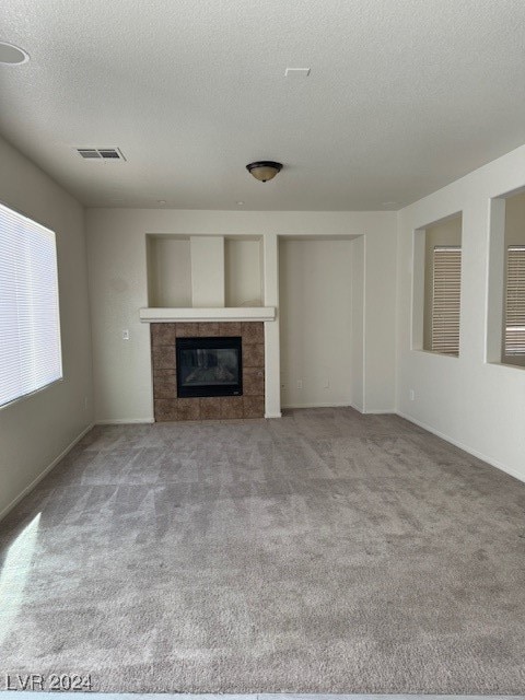 unfurnished living room featuring carpet, a textured ceiling, and a tiled fireplace