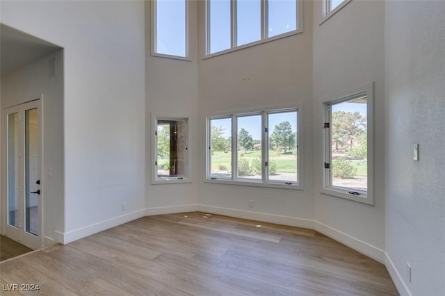 unfurnished room with baseboards, light wood-style floors, and a towering ceiling