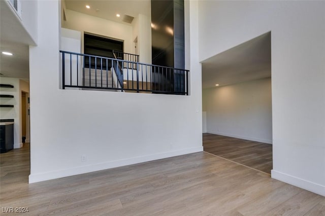 unfurnished room featuring recessed lighting, a high ceiling, baseboards, and wood finished floors