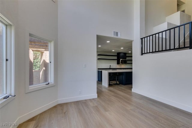 unfurnished living room with visible vents, light wood finished floors, baseboards, a towering ceiling, and stairs