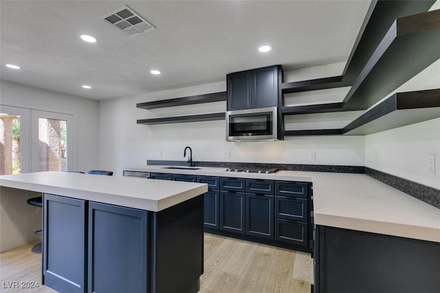 kitchen with open shelves, stainless steel microwave, visible vents, and a sink