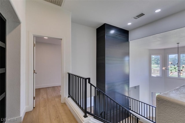 corridor with visible vents, an upstairs landing, a notable chandelier, and wood finished floors