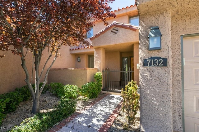 view of exterior entry with a tiled roof, a gate, fence, and stucco siding