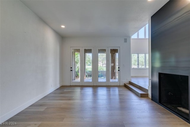 unfurnished living room featuring recessed lighting, baseboards, a large fireplace, and light wood-style flooring