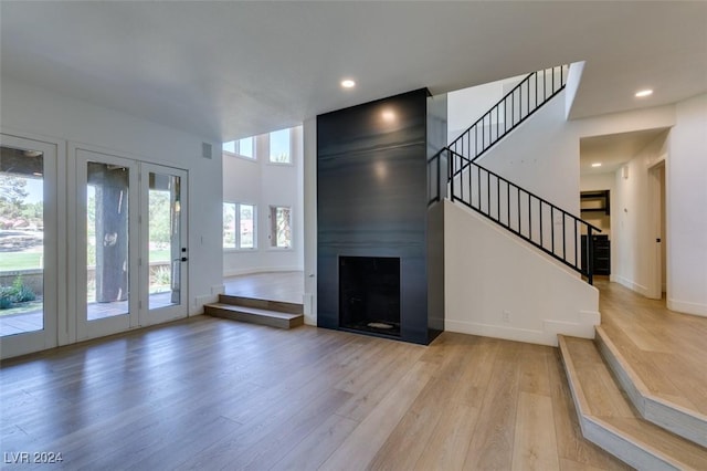 unfurnished living room featuring recessed lighting, a large fireplace, stairs, and light wood finished floors