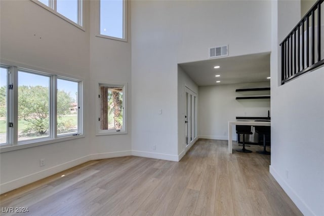 unfurnished living room featuring visible vents, a towering ceiling, baseboards, and wood finished floors