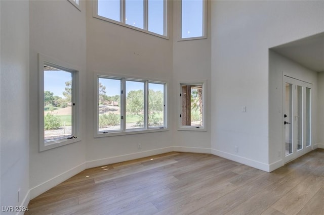 interior space featuring light wood-style flooring, baseboards, and a towering ceiling