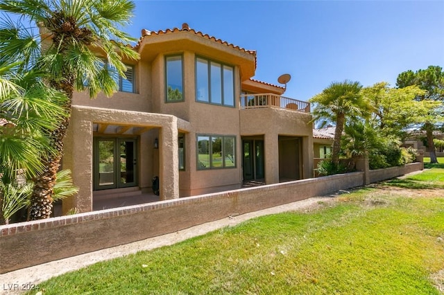 back of property with a tiled roof, stucco siding, french doors, a lawn, and a balcony